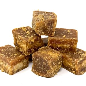 Peut inclure: Plusieurs cubes bruns, probablement du sucre solidifi&eacute; ou une confiserie similaire. Les blocs ont une surface rugueuse et textur&eacute;e. L'arri&egrave;re-plan est blanc.