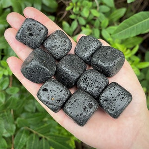 May include: A hand holding a collection of ten small, black, rough, cube-shaped volcanic rocks.