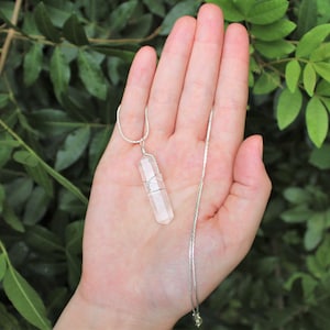 May include: A clear quartz crystal pendant on a silver chain. The crystal is wrapped in silver wire and has a faceted shape.