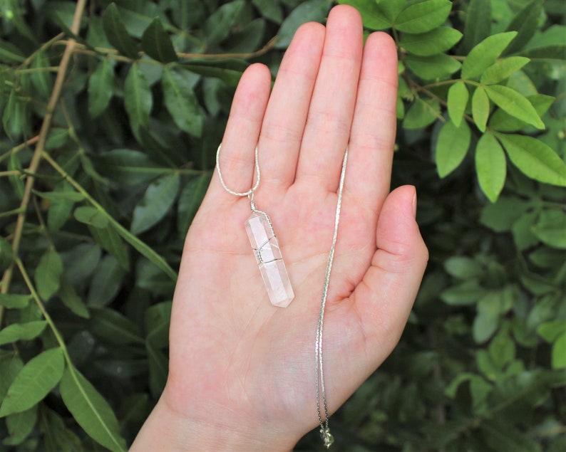 May include: A clear quartz crystal pendant on a silver chain. The crystal is wrapped in silver wire and has a faceted shape.