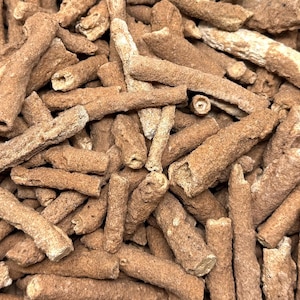 May include: Close-up of a pile of brown, cylindrical objects with a rough, textured surface. The objects have a natural, organic appearance, with some showing hollow interiors. The overall color is a warm, earthy brown.