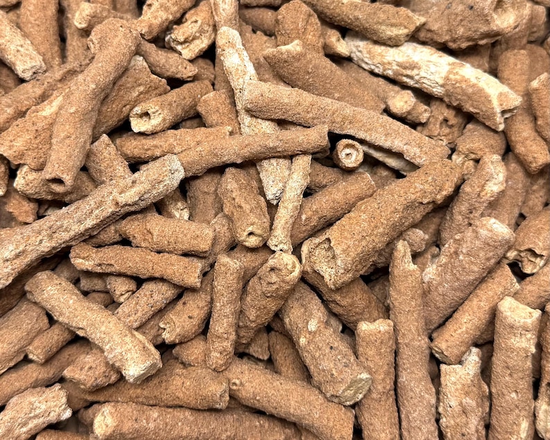May include: Close-up of a pile of brown, cylindrical objects with a rough, textured surface. The objects have a natural, organic appearance, with some showing hollow interiors. The overall color is a warm, earthy brown.