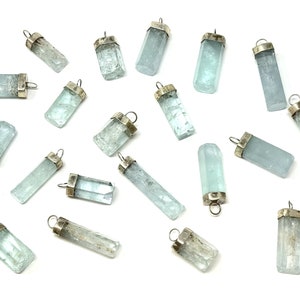 May include: A collection of aquamarine crystal pendants with silver-colored caps and loops. The pendants are various shapes and sizes, displaying a pale blue-green color. The background is white, highlighting the pendants.
