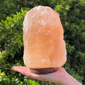 May include: A large, natural Himalayan salt lamp with a warm, orange-pink hue. The lamp is sitting on a wooden base and is lit, casting a soft glow.
