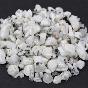 May include: A pile of white moonstone chips with black inclusions. The chips are various sizes and shapes.