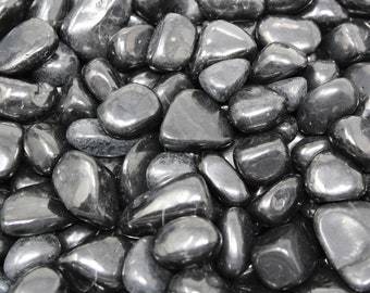 May include: A close-up of a pile of smooth, black polished stones. The stones are various sizes and shapes, and they have a glossy finish.