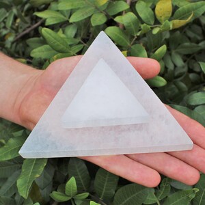 May include: Two stacked white translucent triangular plates made of selenite. The larger base triangle supports a smaller triangle centred on top. Both pieces feature a smooth, flat surface with a crystalline texture and straight edges.