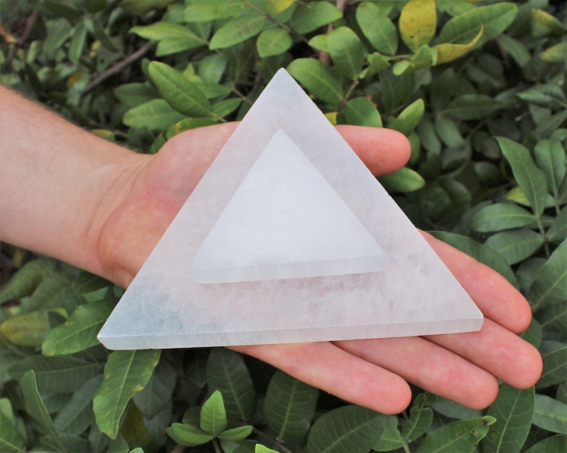 May include: Two stacked white translucent triangular plates made of selenite. The larger base triangle supports a smaller triangle centred on top. Both pieces feature a smooth, flat surface with a crystalline texture and straight edges.