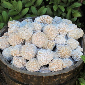 K&ouml;nnte beinhalten: Ein Holzfass gef&uuml;llt mit einer gro&szlig;en Sammlung von Rosenquarzkristallen. Die Kristalle sind hellrosa und haben eine raue, strukturierte Oberfl&auml;che.