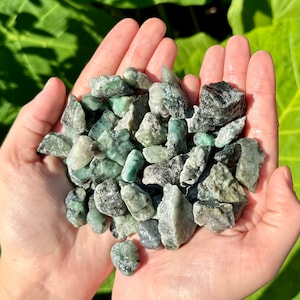 May include: A handful of green emerald gemstone chips. The chips are various sizes and shapes, with some having a more opaque appearance.
