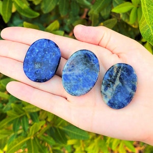Op de afbeelding: Drie gladde, ovale, gepolijste lapis lazuli stenen. De stenen zijn diepblauw met witte en gouden aderen die er doorheen lopen.