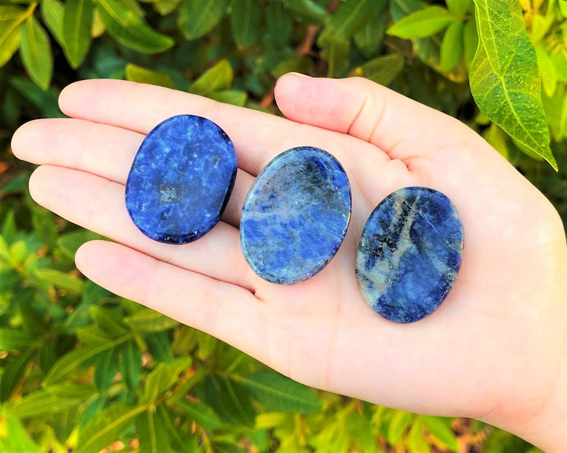 Op de afbeelding: Drie gladde, ovale, gepolijste lapis lazuli stenen. De stenen zijn diepblauw met witte en gouden aderen die er doorheen lopen.