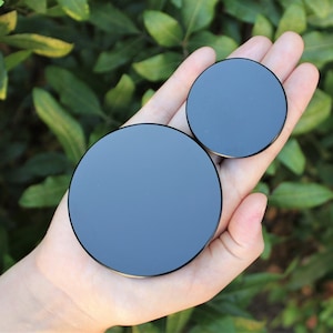 May include: Two black round phone grips of different sizes. The larger grip is in the palm of a hand, and the smaller grip is on top of the larger grip.