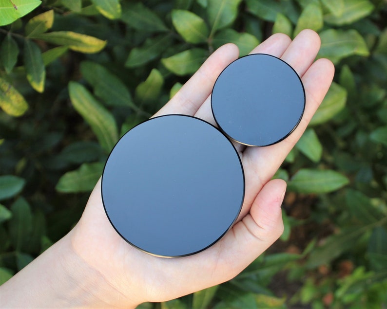 May include: Two black round phone grips of different sizes. The larger grip is in the palm of a hand, and the smaller grip is on top of the larger grip.