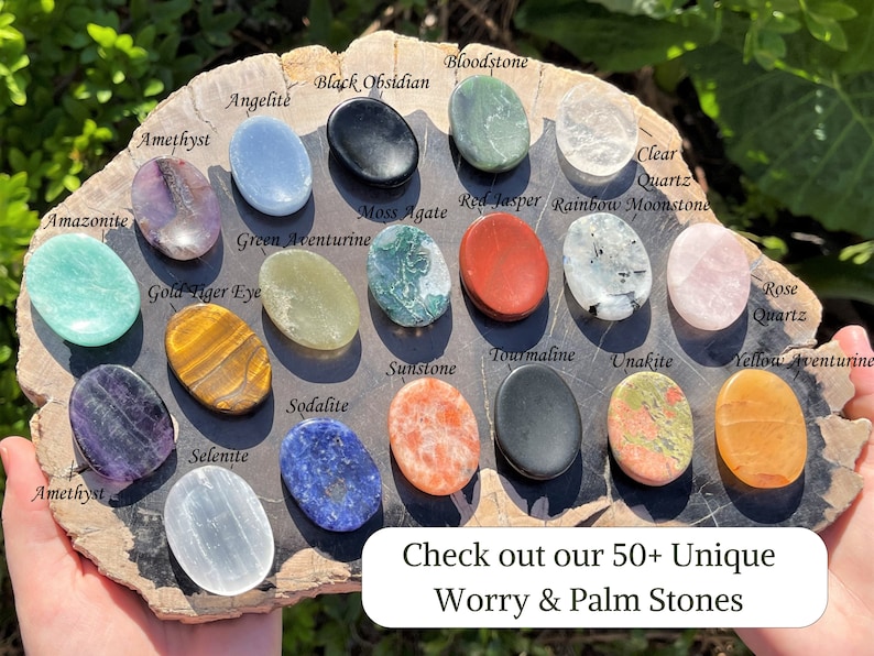 Op de afbeelding: Een assortiment van 16 worry- of palmstenen in verschillende kleuren en texturen, waaronder amethist, groene aventurijn, tijgeroog, sodaliet, rozenkwarts en helder kwarts. De stenen zijn in een cirkel op een houten oppervlak gerangschikt. De tekst "Ontdek onze 50+ unieke worry- en palmstenen" is zichtbaar onderaan de afbeelding.