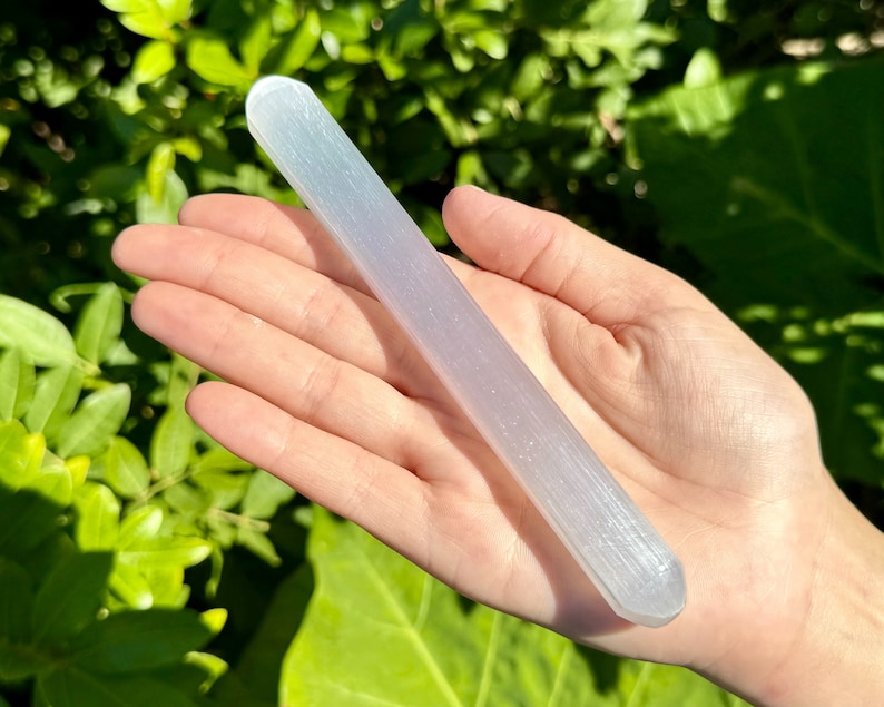 May include: A white selenite wand with a smooth, polished surface. The wand is approximately 6 inches long and has a rounded end.