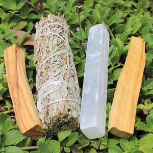 May include: Three smudge sticks for cleansing rituals. A white sage bundle, a palo santo stick, and a selenite stick.