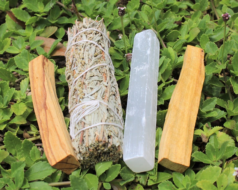 May include: Three smudge sticks for cleansing rituals. A white sage bundle, a palo santo stick, and a selenite stick.