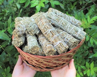 May include: A wicker basket filled with bundles of sage smudge sticks. The sage is tied together with twine and is a light green color.