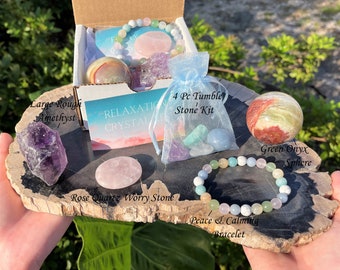 May include: A crystal kit with a large rough amethyst, a green onyx sphere, a rose quartz worry stone, a 4 piece tumbled stone kit, and a peace and calming bracelet. The kit is packaged in a brown box with a blue and white patterned bag.