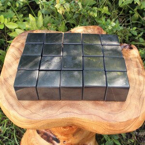 May include: Twenty-five black obsidian cubes arranged in a grid pattern on a wooden surface. The cubes are polished and reflect light.