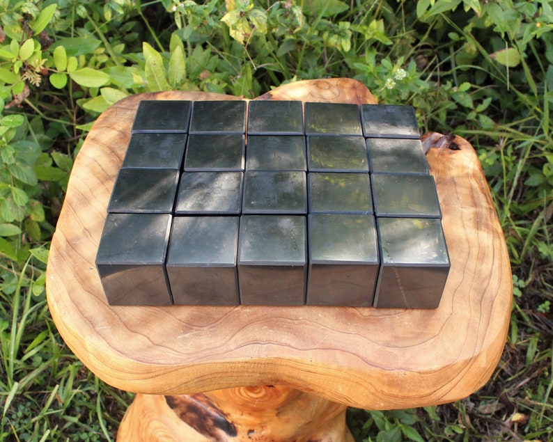 May include: Twenty-five black obsidian cubes arranged in a grid pattern on a wooden surface. The cubes are polished and reflect light.