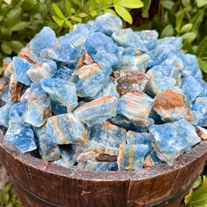 May include: A large pile of blue and brown calcite crystals in a wooden bowl. The crystals are rough and have a natural, unpolished look.