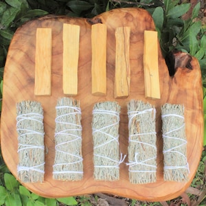 May include: A wooden board with six bundles of sage smudge sticks and six sticks of palo santo wood. The sage bundles are tied with white string and the palo santo sticks are a light brown color.
