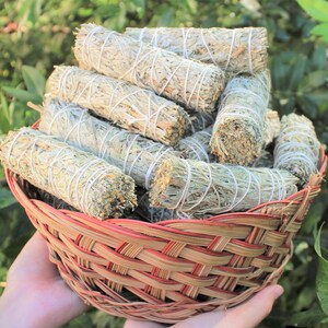 May include: A wicker basket filled with bundles of white sage smudge sticks. The sticks are tied with twine and have a natural, earthy look.