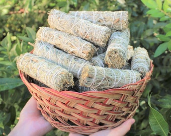 May include: A woven basket filled with bundles of sage smudge sticks. The sticks are tied with white string and have a light green color.
