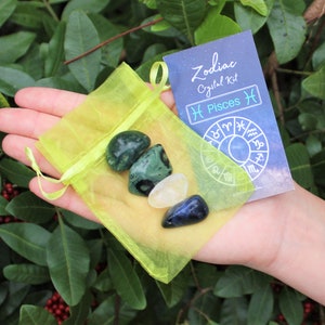 K&ouml;nnte beinhalten: Eine gelbe Organza-Tasche gef&uuml;llt mit drei Kristallen: einem gr&uuml;nen Aventurin, einem klaren Quarz und einem blauen Sodalith. Eine Karte mit dem Text "Zodiac Crystal Kit Pisces ♓" und einem Tierkreisrad ist sichtbar.