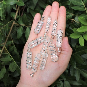May include: A collection of clear quartz crystal points wrapped in silver wire. The crystals are all different sizes and shapes, and they are arranged in a hand.