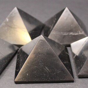 May include: Six black obsidian pyramids of varying sizes arranged in a semi-circle on a gray surface.