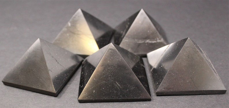 May include: Six black obsidian pyramids of varying sizes arranged in a semi-circle on a gray surface.