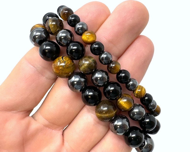 Pode incluir: Tr&ecirc;s pulseiras sobrepostas com contas pretas, olho de tigre e hematita.