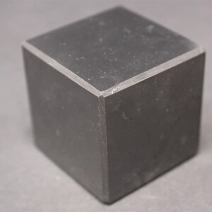May include: A black cube with a smooth, slightly textured surface. The cube has sharp edges and corners.