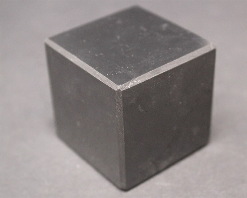 May include: A black cube with a smooth, slightly textured surface. The cube has sharp edges and corners.