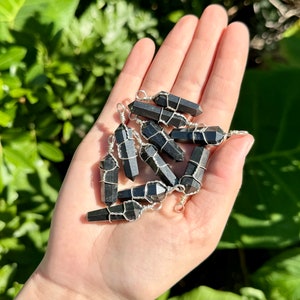 May include: A collection of black obsidian crystal points wrapped in silver wire. The points are all different sizes and shapes, and they are arranged in a pile on a hand.