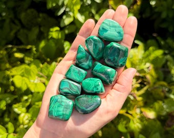 May include: A collection of ten polished malachite stones with distinct banded patterns in various shades of vibrant green. Each stone features a smooth, rounded surface with unique swirling dark and light green mineral layers visible throughout.