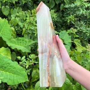 May include: A tall, polished stone tower with a hexagonal base and a pointed top. The stone features translucent layers of pale green and white, accented by prominent, jagged veins of deep orange and brown running vertically through the structure.