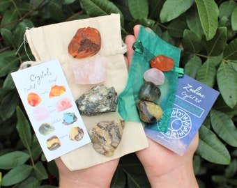 May include: A set of crystals for the zodiac sign Taurus, in a small green pouch and a white pouch. The crystals are carnelian, rose quartz, aventurine, tiger's eye, and clear quartz. The card says "Zodiac Crystal Kit Taurus".