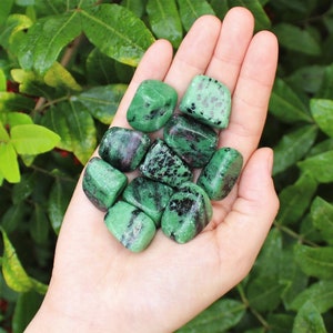 May include: A collection of green and black tumbled stones. The stones are smooth and have a speckled appearance.
