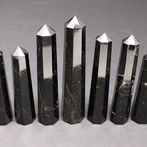 May include: Eight black obsidian crystal points with a polished finish. The points are arranged in a row, with the largest point in the center.