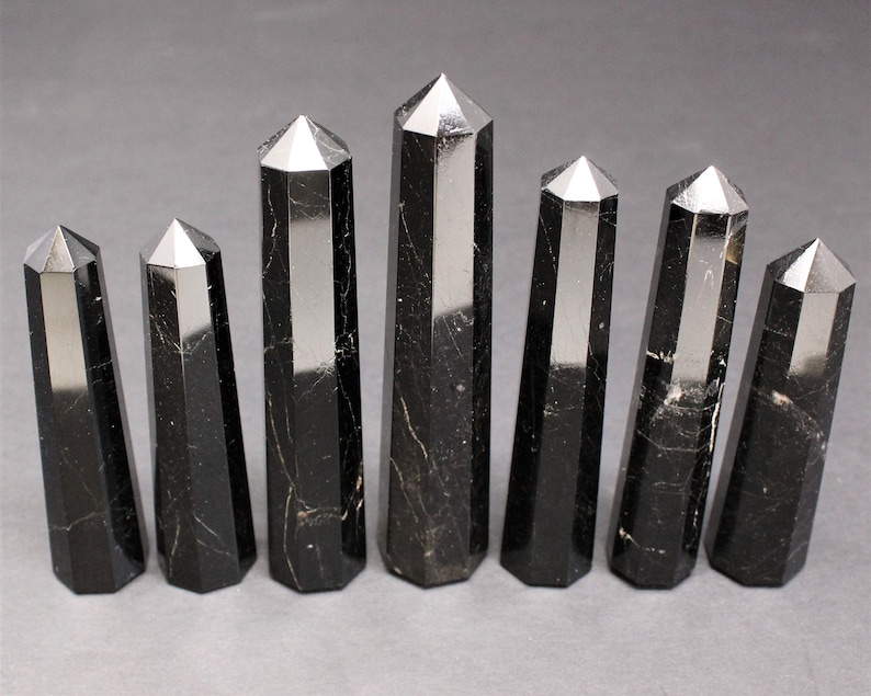 May include: Eight black obsidian crystal points with a polished finish. The points are arranged in a row, with the largest point in the center.