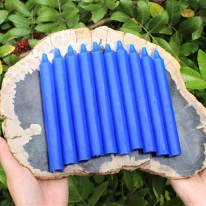 May include: A set of twelve blue taper candles arranged on a wooden slab. The candles are approximately 7 inches long.