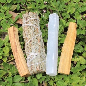 May include: A bundle of white sage, a stick of palo santo wood, and a white selenite crystal stick. These items are commonly used for smudging and cleansing rituals.