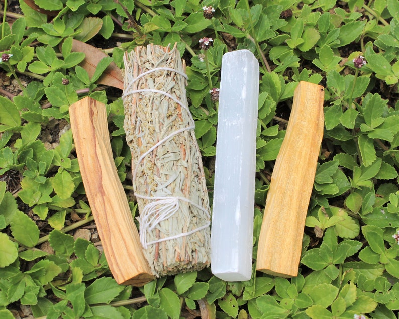 May include: A bundle of white sage, a stick of palo santo wood, and a white selenite crystal stick. These items are commonly used for smudging and cleansing rituals.
