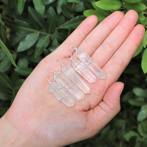 May include: Five clear quartz crystal points wrapped in silver wire with a loop at the top for hanging. The crystals are arranged in a row on a hand.