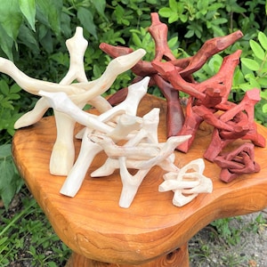 May include: A collection of interlocking wooden display stands in light beige and reddish-brown finishes. These tripod-style stands feature three carved legs that cross at the center to create a stable base for holding spherical objects or other items.