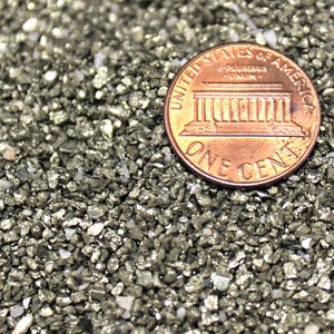 May include: A close-up of a US penny coin resting on a bed of small, metallic, gray-colored rocks. The coin features the Lincoln Memorial and the inscription "United States of America, E Pluribus Unum, One Cent".